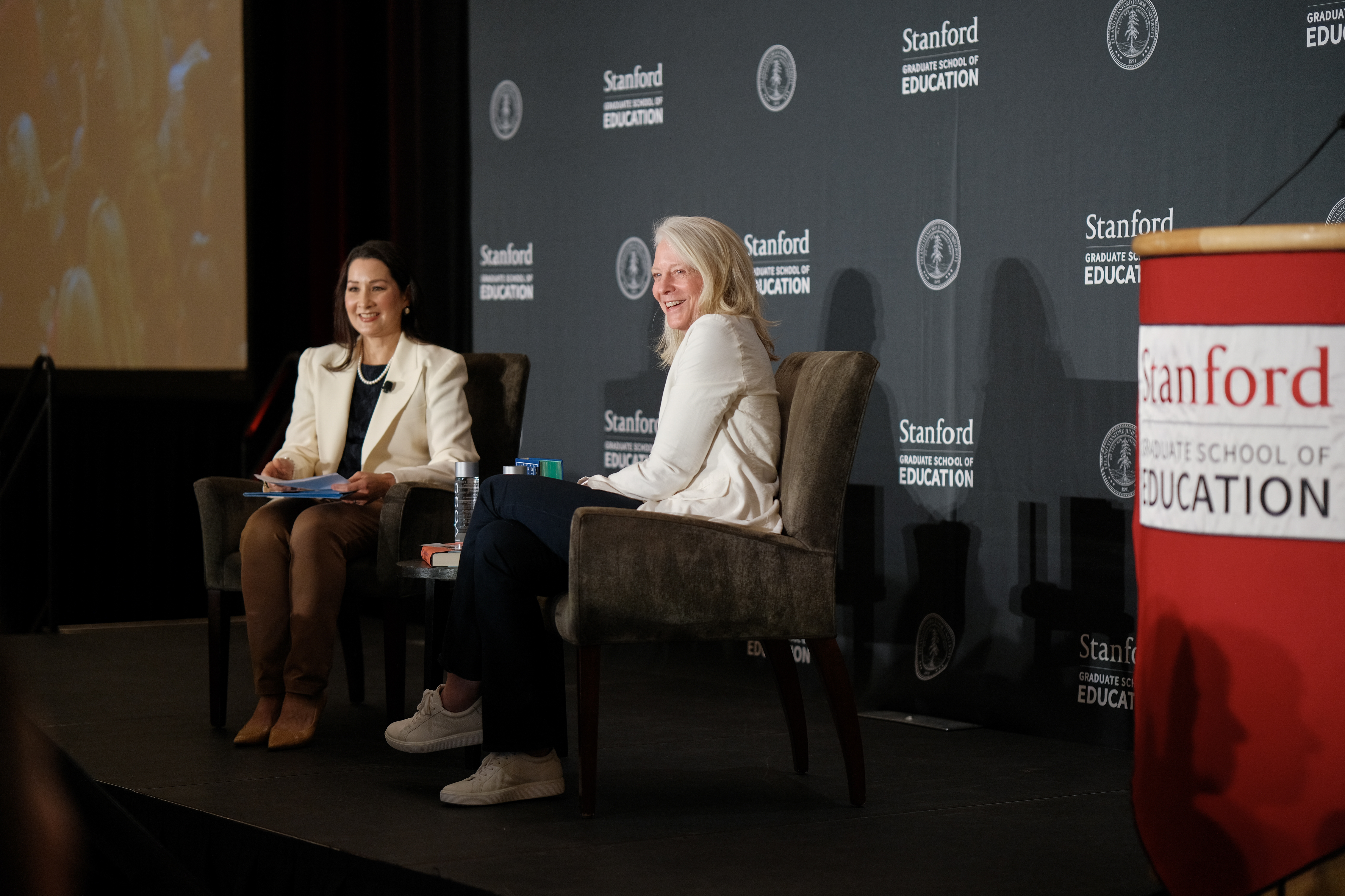 Photo of Bonnie Garmus and Christine Min Wotipka sitting on stage looking out to the audience