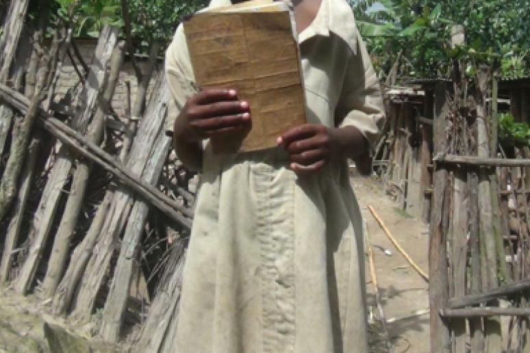 Flora holds the only book she could find in her home. She uses the same book for Kinyarwanda, Maths and English.