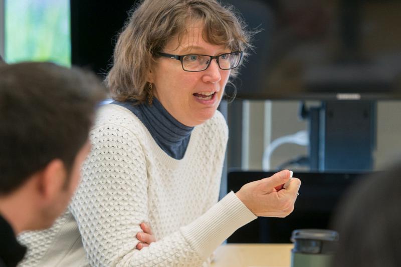 Professor sitting at a desk speaking to the audience
