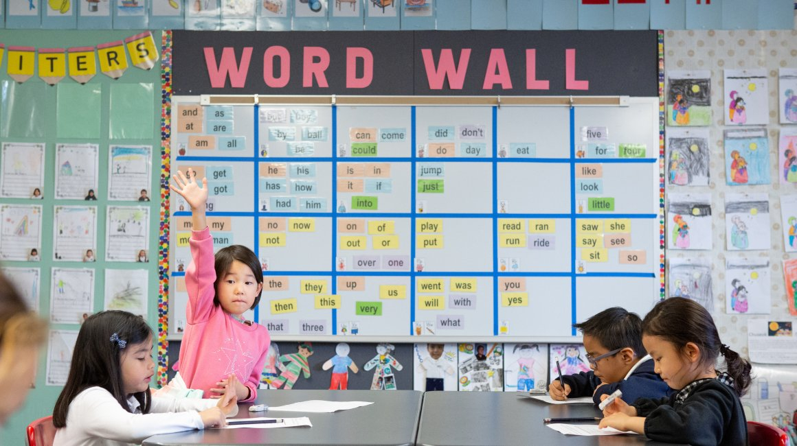 A kindergarten student raises her hand in a dual-language immersion class.