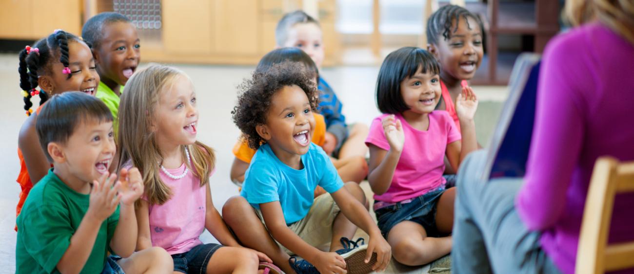 Young school children smiling at the teacher reading.