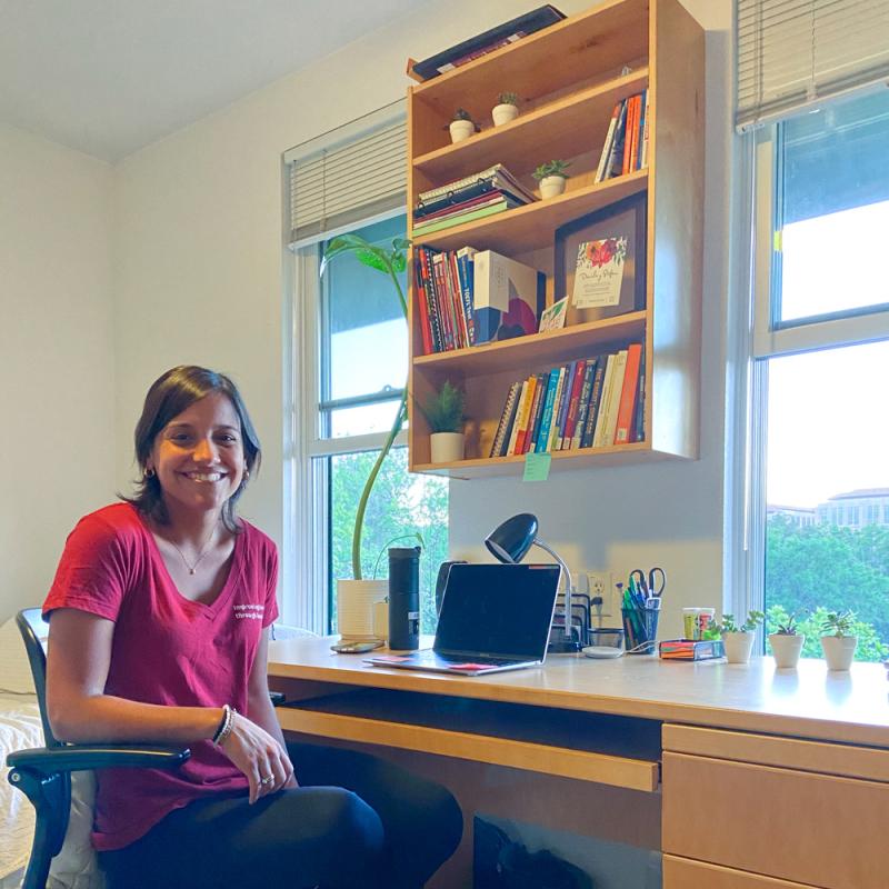 Daniela Gamboa in her apartment on campus, sitting at a desk and smiling