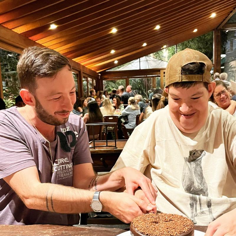 GSE assistant professor Guilherme Lichand (left) cuts cake with his brother Bruno.