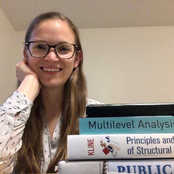 Madison Dell with a stack of books for her doctoral studies, smiling